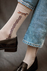 Chaussettes de couleur gris clair au motif mosaïque avec un liseré doré représentant un oiseau. En 85% fil d'écosse, 13% polyamide et 2% élasthanne. Modèle de mi-mollet (courtes) pour femme de la marque Daphné. Fines et légères. Pointures : du 36 au 41